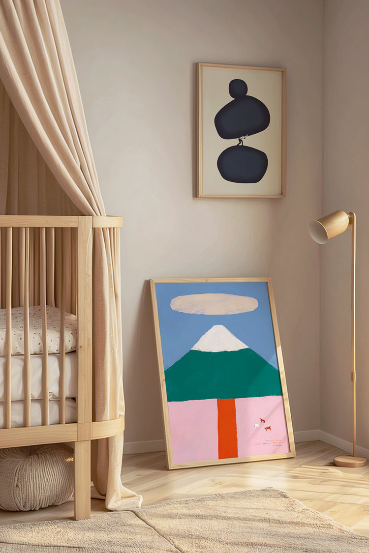 A imagem apresenta um quarto infantil com dois quadros, sendo um na parede e um no chão. Ambos com moldura em madeira clara. Um deles apresenta a ilustração de uma montanha, em verde e branco, com um céu azul e um campo em rosa e vermelho com alguns animais. O segundo quadro apresenta a colagem de um homem carregando um peso sobre os ombros.
