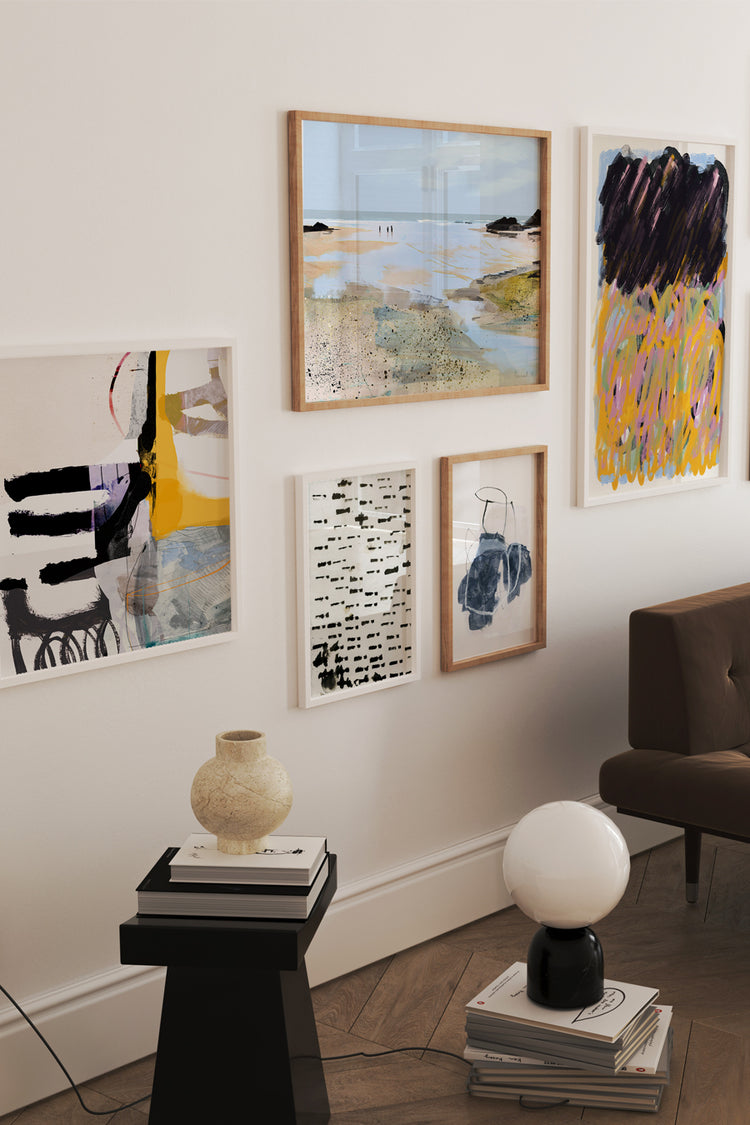 Composição de quadros variados em parede de sala com decoração contemporânea. As obras mesclam paisagens, arte abstrata e ilustração gráfica, criando uma galeria harmoniosa acima de sofá marrom.