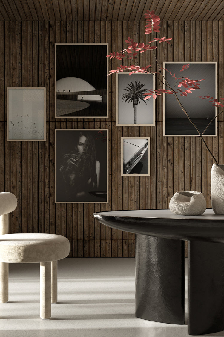 Composição sofisticada de quadros em preto e branco sobre parede de madeira ripada. Sala com mesa escultural preta, cadeira estofada clara e vasos com folhagens secas, em estilo contemporâneo e elegante.