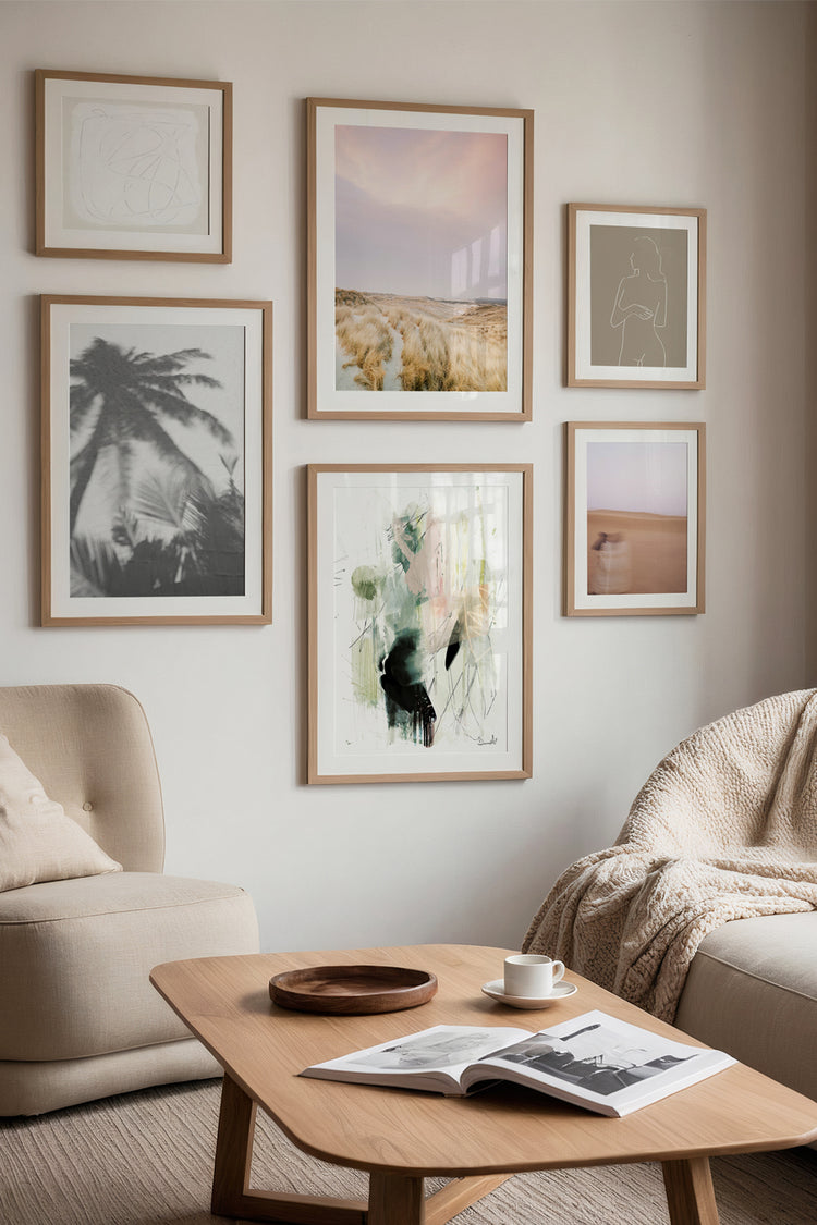 Sala com decoração suave e composição de quadros em tons neutros, mesclando arte abstrata, fotografias e ilustrações. Ambiente acolhedor com poltrona, manta, mesa de madeira e luz natural.