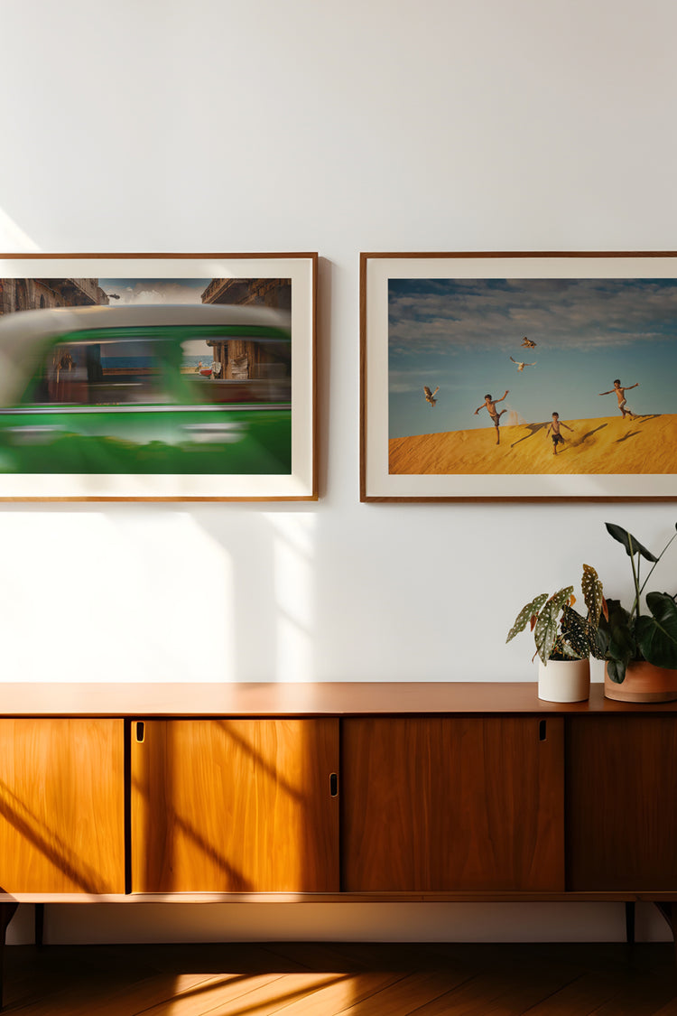 Paredes decoradas com fotografias artísticas de paisagens tropicais e cenas urbanas em movimento – decoração com quadros modernos sobre aparador de madeira vintage em ambiente iluminado e com plantas naturais.