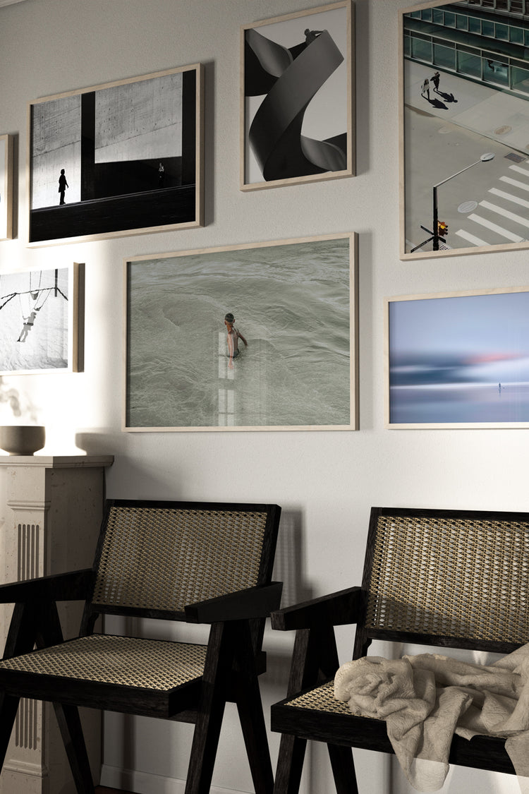 Sala com atmosfera contemporânea e acolhedora, destacando uma galeria com sete quadros de fotografias artísticas em diferentes estilos — desde retratos urbanos até composições minimalistas e abstratas. Abaixo, duas cadeiras de madeira escura com palhinha e um cobertor jogado trazem aconchego ao ambiente.
