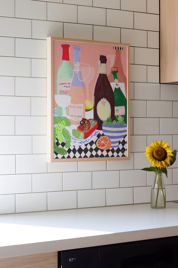 Arte colorida de garrafas e frutas com fundo rosa emoldurada na cozinha com azulejos brancos e girassol em vaso.