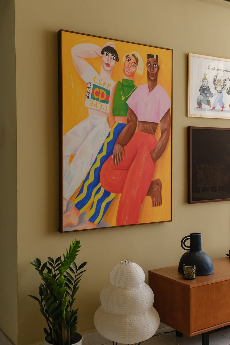 Parede amarela em sala de estar com móveis em cor de madeira. Na parede, há um quadro do artista Cépé, da Obrah, de três pessoas encostadas em uma parede. Ilustração despojada e colorida.