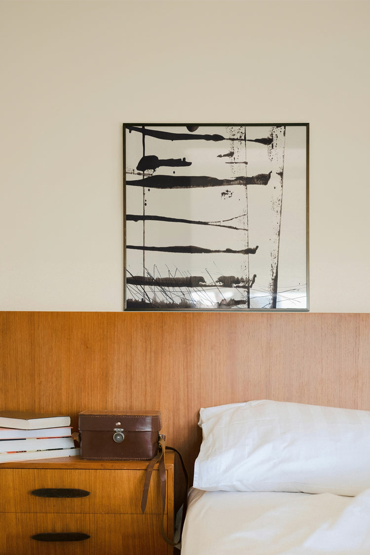 Quadro preto e branco abstrato com linhas verticais sobre cama de madeira em quarto minimalista.