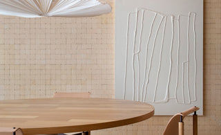 Ambiente com mesa de jantar de madeira, duas cadeiras também de madeira e lustre pendente branco. Ao fundo, um qua