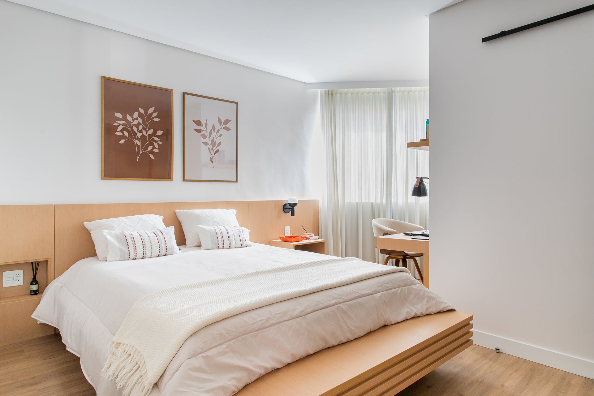 quarto decorado por escritório de arquitetura brenda amaral com quadros decorativos da obrah. O ambiente possui tonalidades claras e amadeiradas e os quadros são ilustrativos de folhagens