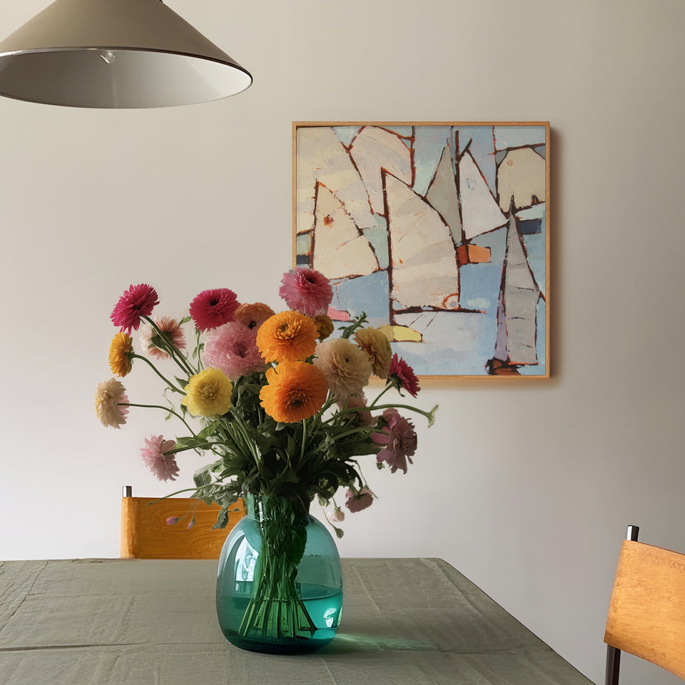 
"Quadro com pintura abstrata náutica em tons claros na parede de sala de jantar com mesa posta, vaso verde de vidro com buquê de flores coloridas e cadeiras de madeira. Decoração artística e aconchegante com toque floral e marítimo.
